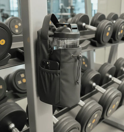 Magnetic gym bag holding a water bottle and phone, attached to gym equipment near dumbbells